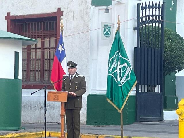 Un carabinero habla desde un atril, entre la bandera de Chile y el estandarte verde